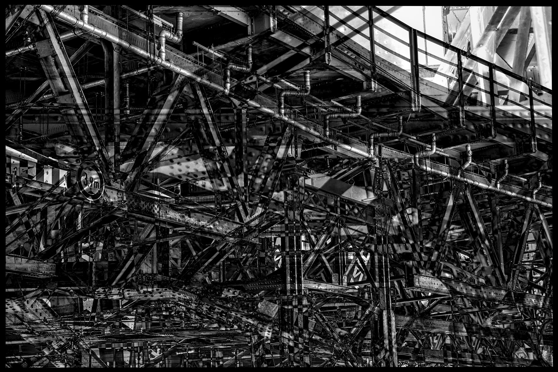 A steel bridge with confusing substructure constructions. Riveted and bolted iron girders condense into a technical labyrinth through the fusion of several snapshots.