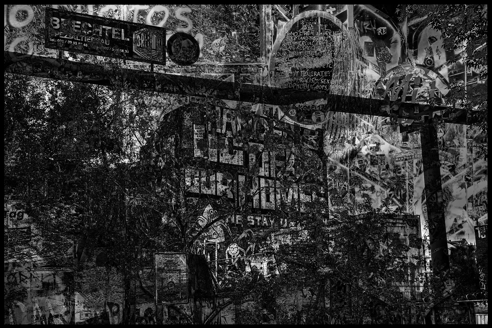 On a house façade further back, a call to action is painted in large letters. Street signs and fences covered with posters create a jungle of image textures in the superimposition of multiple exposures.