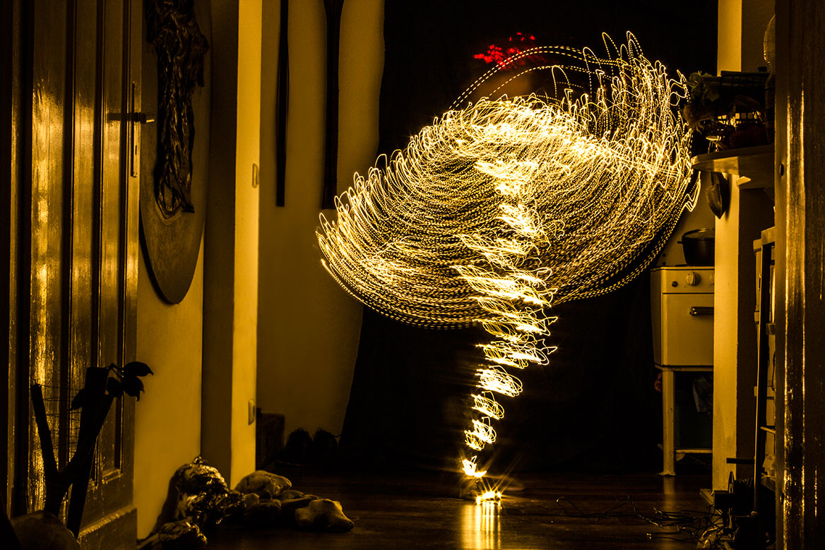 Photographic light staging, setting 3. A woman shines through traces of light that trace the body movements through long exposure. The light traces become more filigree and overlap more strongly.
