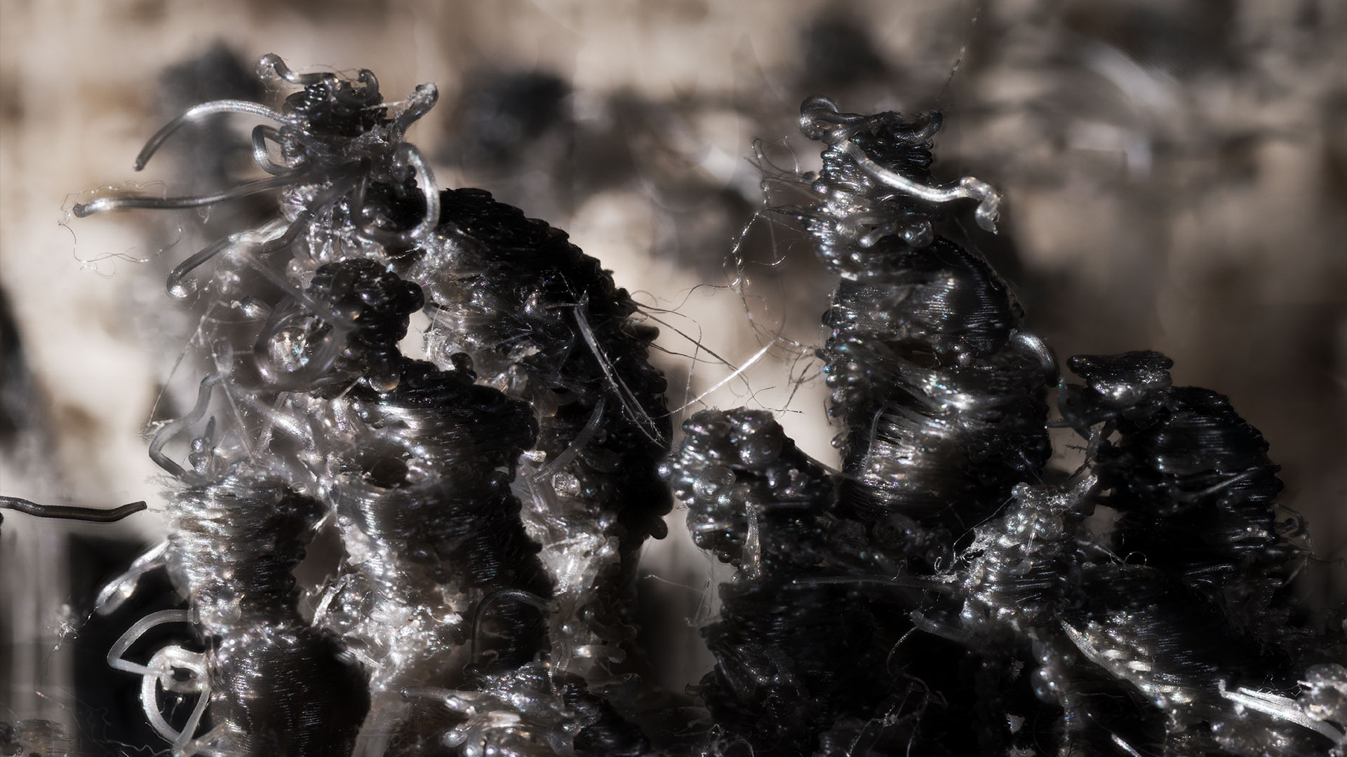 Wie beim vohergehenden Bildausschnitt sind auch hier die Makro-Details der 3D-Druckausgabe klar zu sehen. Die abgebildeten, abstrahierten Figuren von Kriegsopfern sind stark verformt und verfremdet. Die dunklen Figuren stehen vor den hellen Fassaden zerbombter Häuser, die im Hintergrund angedeutet sind.