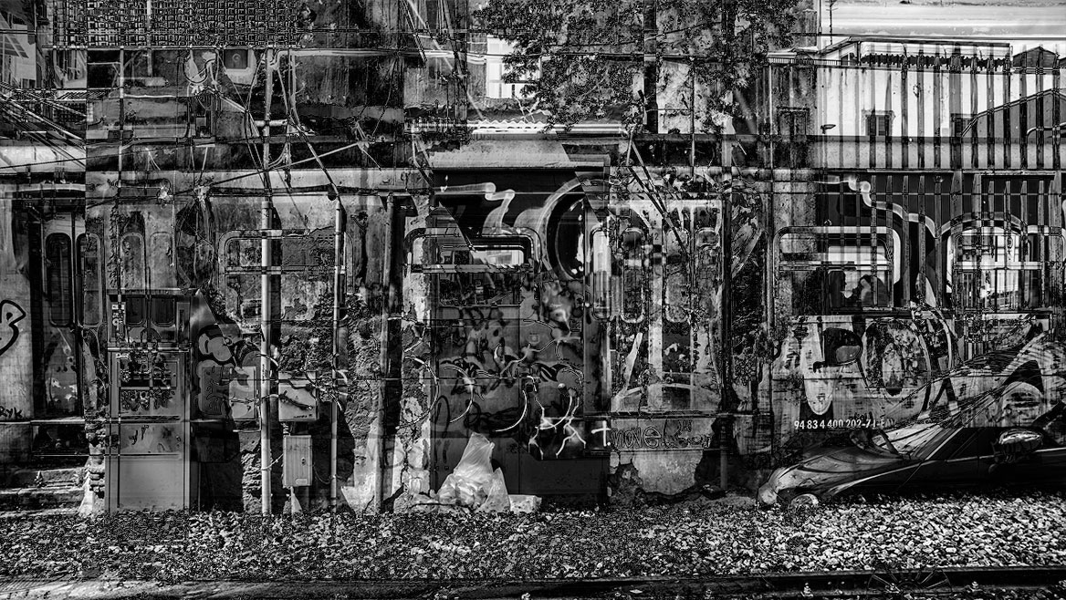 Das künstlerische Schwarz-Weiss-Foto zeigt Fassadenelemente und Eisenbahnwagen-Flächen. Graffiti und Tags überlagern die destruktive Szenerie.