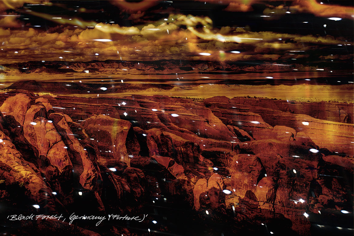 Künstlerische Fotografie: Vogelperspektive einer zerfurchten Gebirgslandschaft mit tiefen Einschnitten vor dramatischer Himmelskulisse.